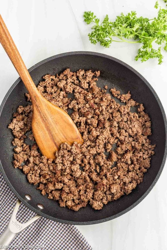 Cooked ground beef in a large skillet with a wooden spoon.