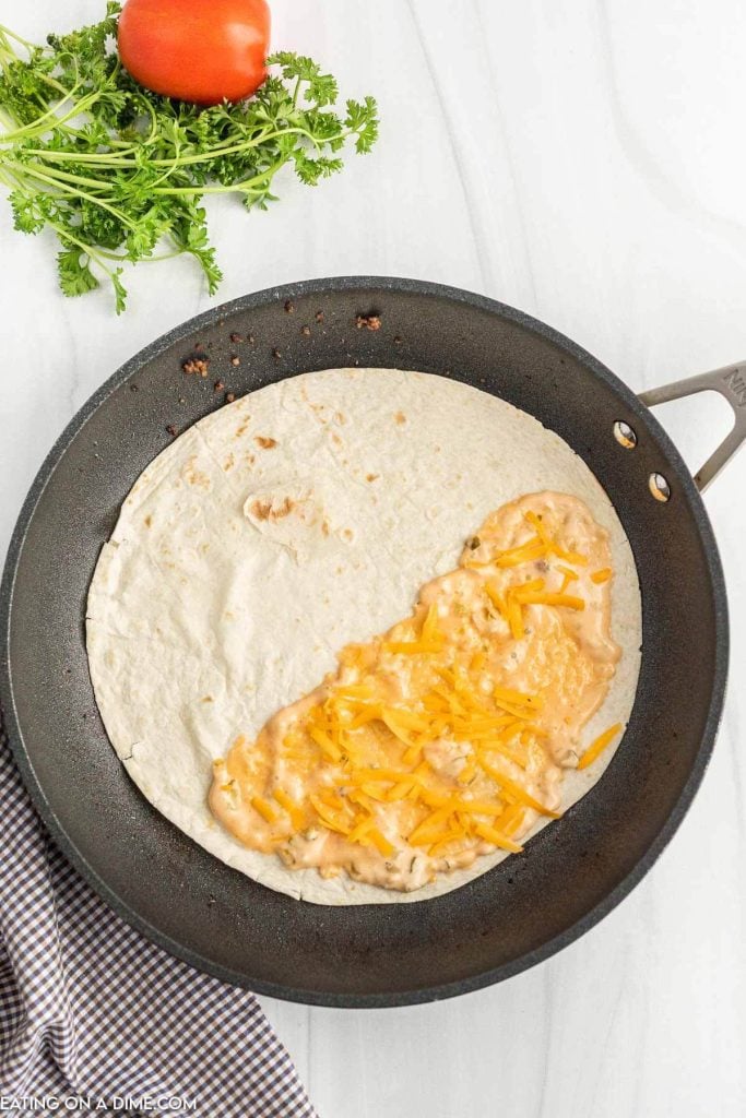 Large flour tortilla in a skillet topped with sauce and shredded cheese.