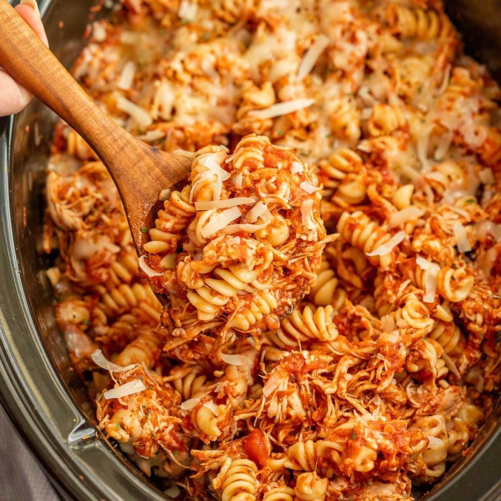 Chicken Parmesan Pasta in the slow cooker with a wooden spoon. 