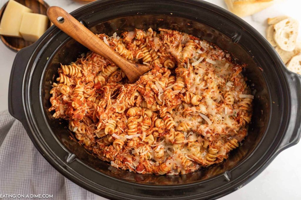 Chicken Parmesan Pasta in the slow cooker with a wooden spoon. 