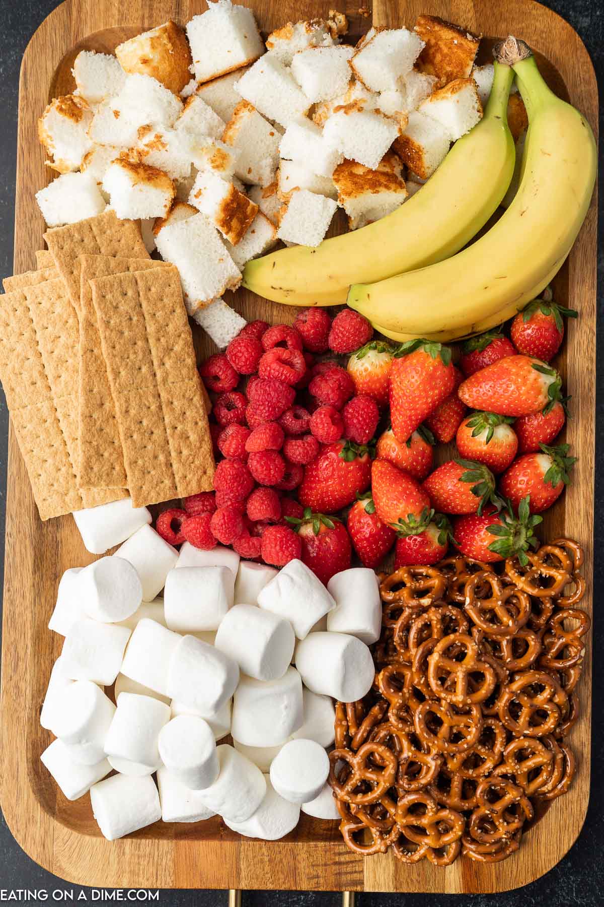 Platter of angel food cake, bananas, graham crackers, strawberries, raspberries, pretzels, and marshmallows