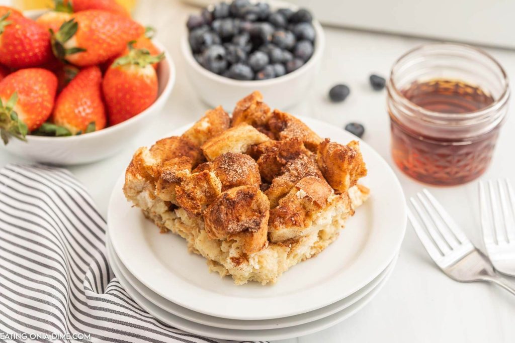 French toast casserole on a white plate with a bowl of strawberries and blueberries