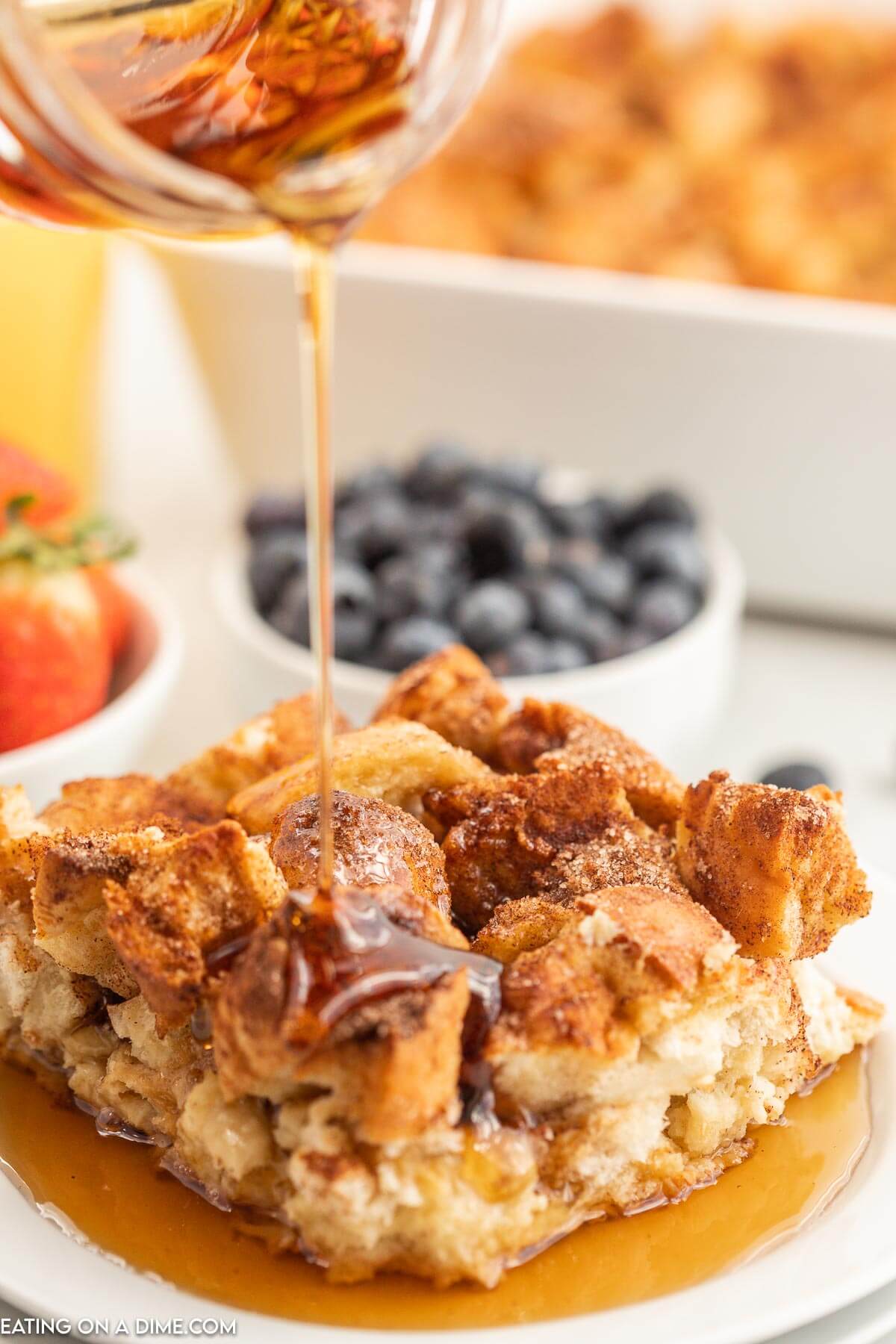 French toast casserole on a white plate with a bowl of strawberries and blueberries