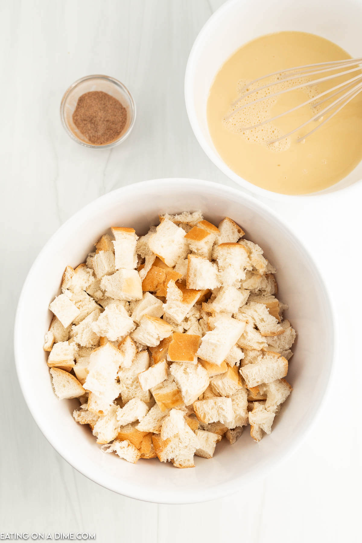 Bread cubes in a bowl with a bowl of egg mixture on the side