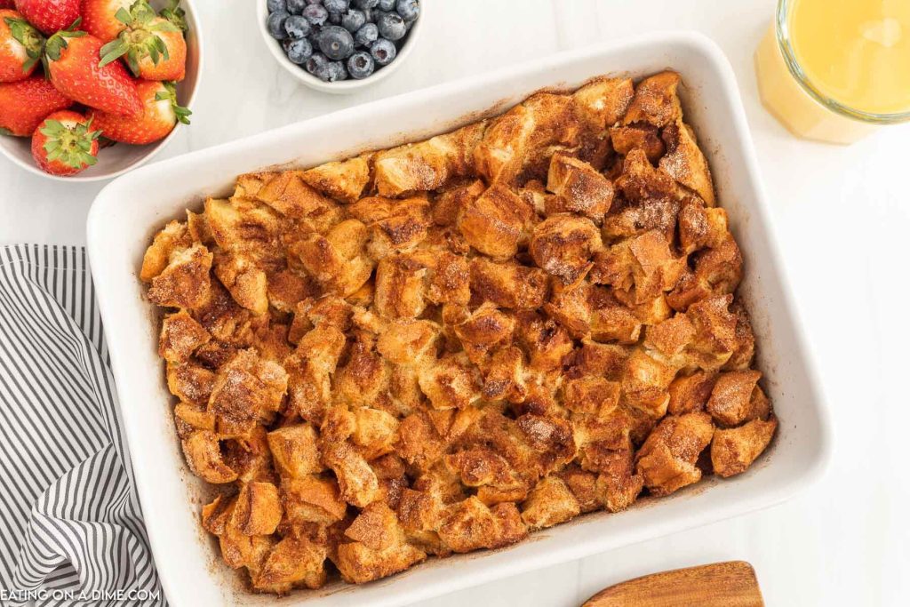 French toast casserole on a white baking dish with a bowl of strawberries and blueberries