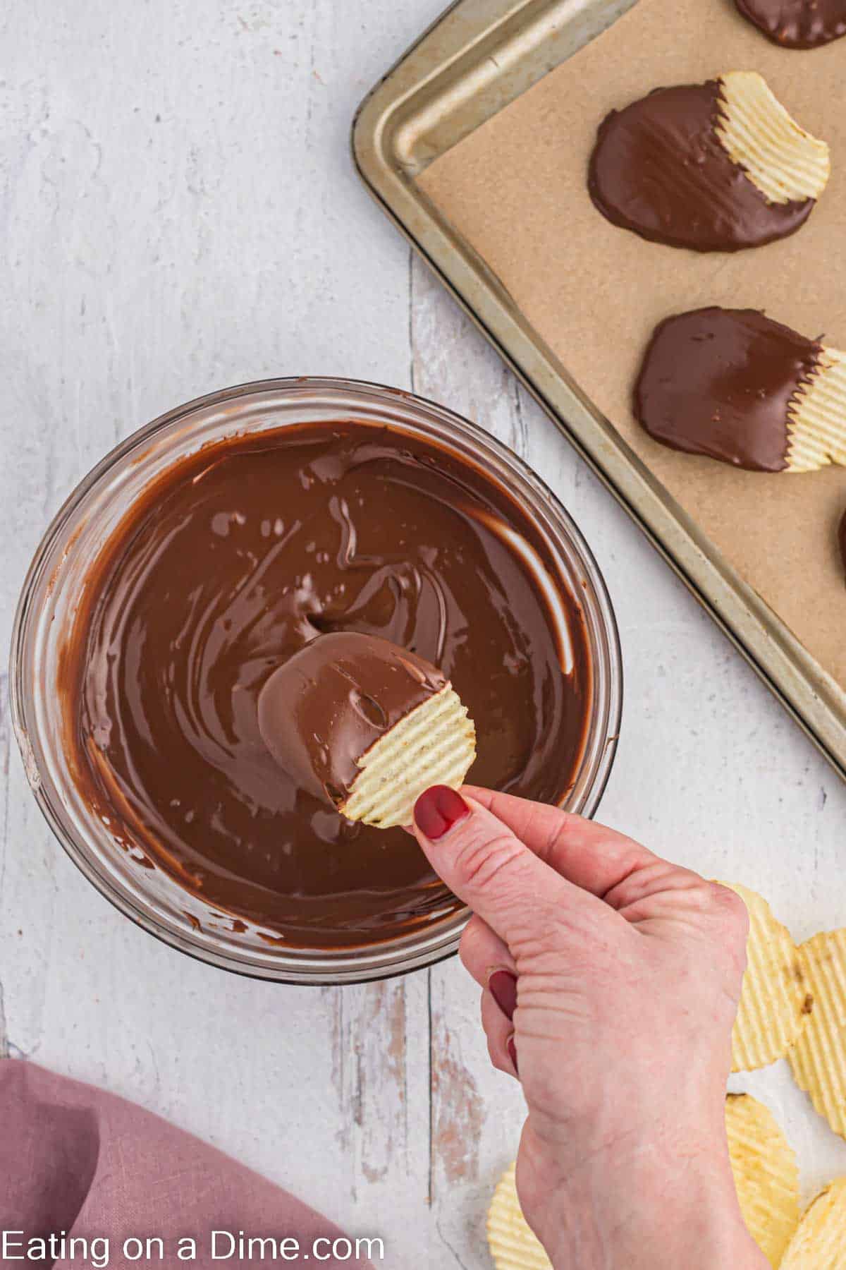 Melting chocolate in a bowl with a potato chip being dipped into the melted chocolate