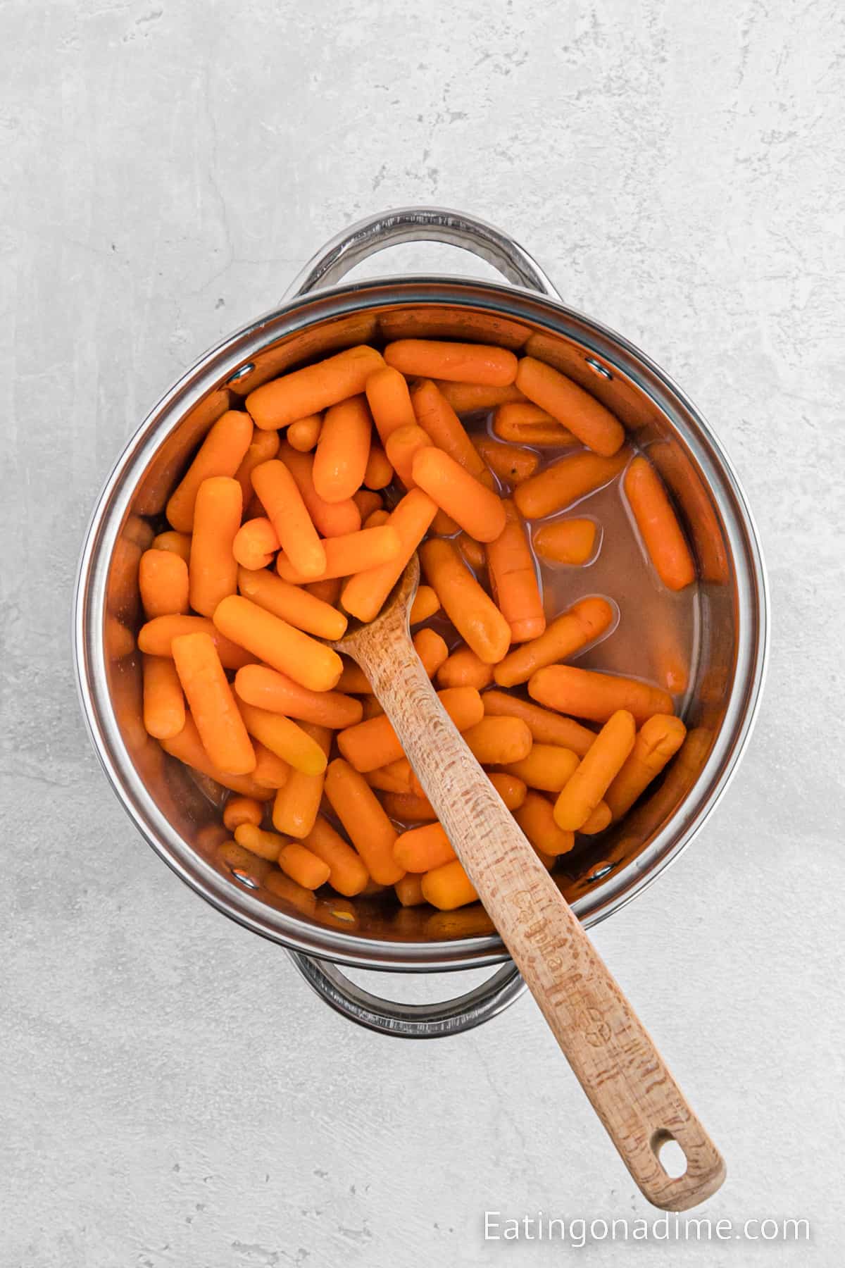 Baby Carrots in a large pot of water with a wooden spoon
