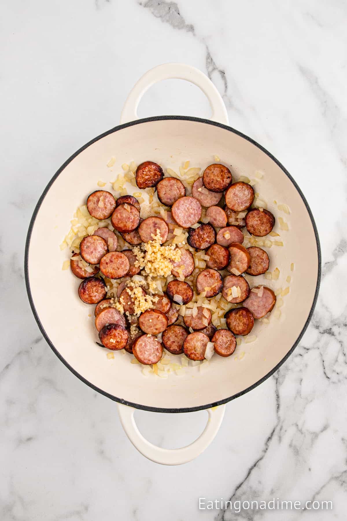 Topping the cooked sausage and onions with minced garlic