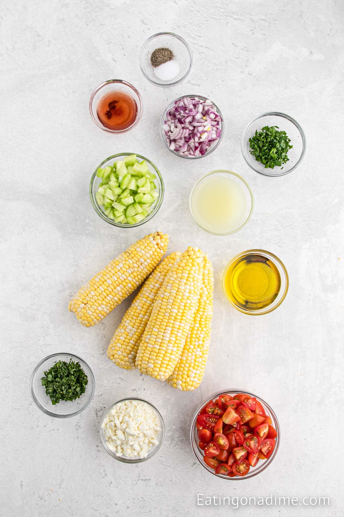 Ingredients needed to make corn salad - corn kernels, cherry tomatoes, small cucumber, red onion, fresh basil, fresh parsley, feta cheese, olive oil, red wine vinegar, salt and pepper