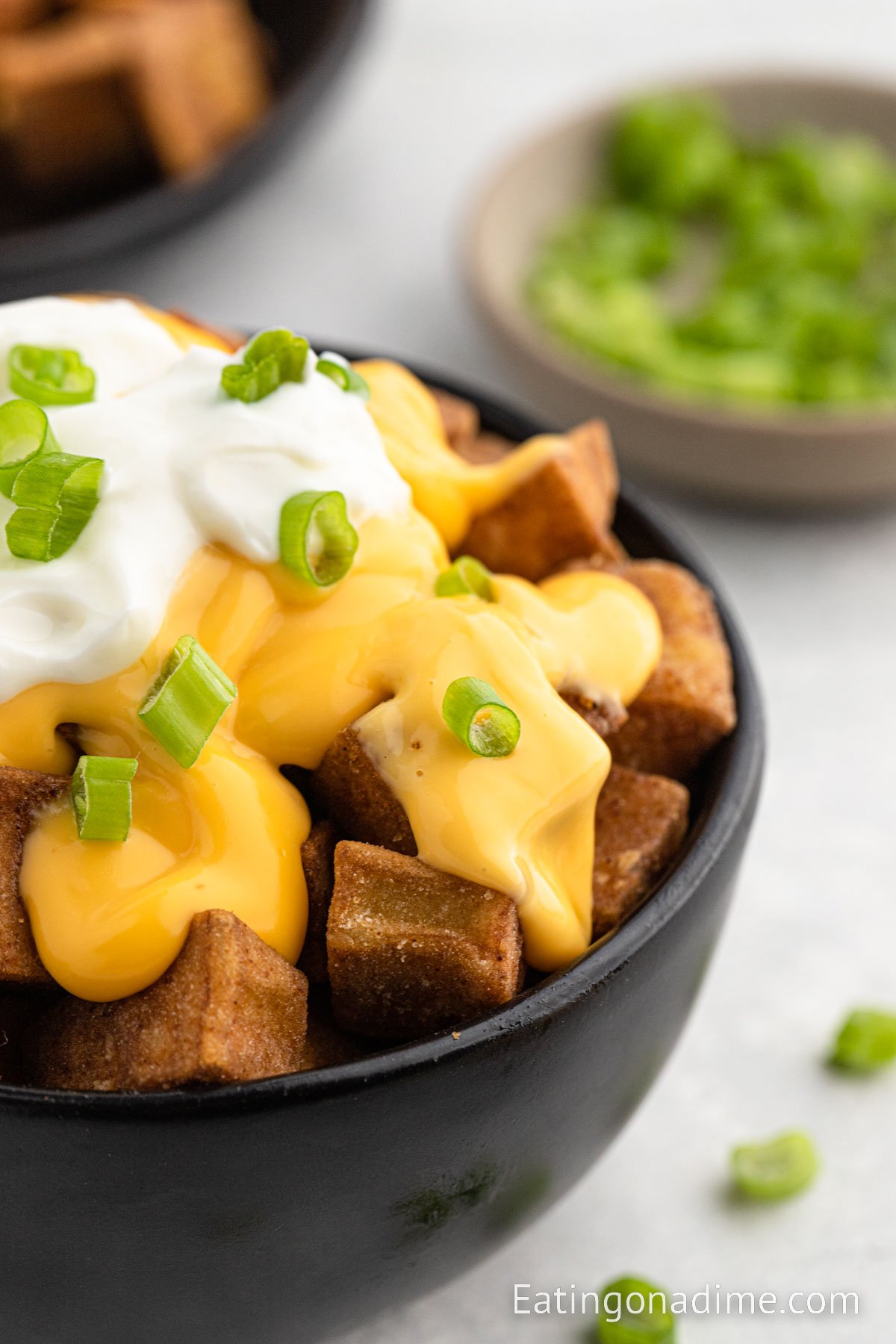 A bowl of cheesy fiesta potatoes topped with cheese, sour cream and chives