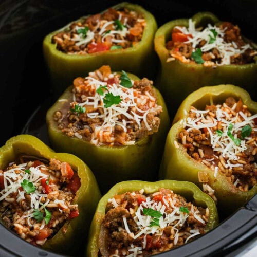 Six green bell peppers stuffed with a savory blend of ground meat, rice, and tomatoes, topped with shredded cheese and parsley—an easy crock pot stuffed peppers recipe perfect for a delicious, hands-off meal.