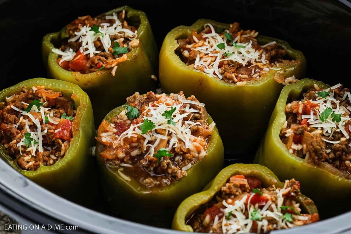 Six green bell peppers are stuffed with ground meat, rice, diced tomatoes, and carrots, topped with cheese and parsley. This crock pot stuffed peppers recipe is ready to be cooked to perfection in your slow cooker.
