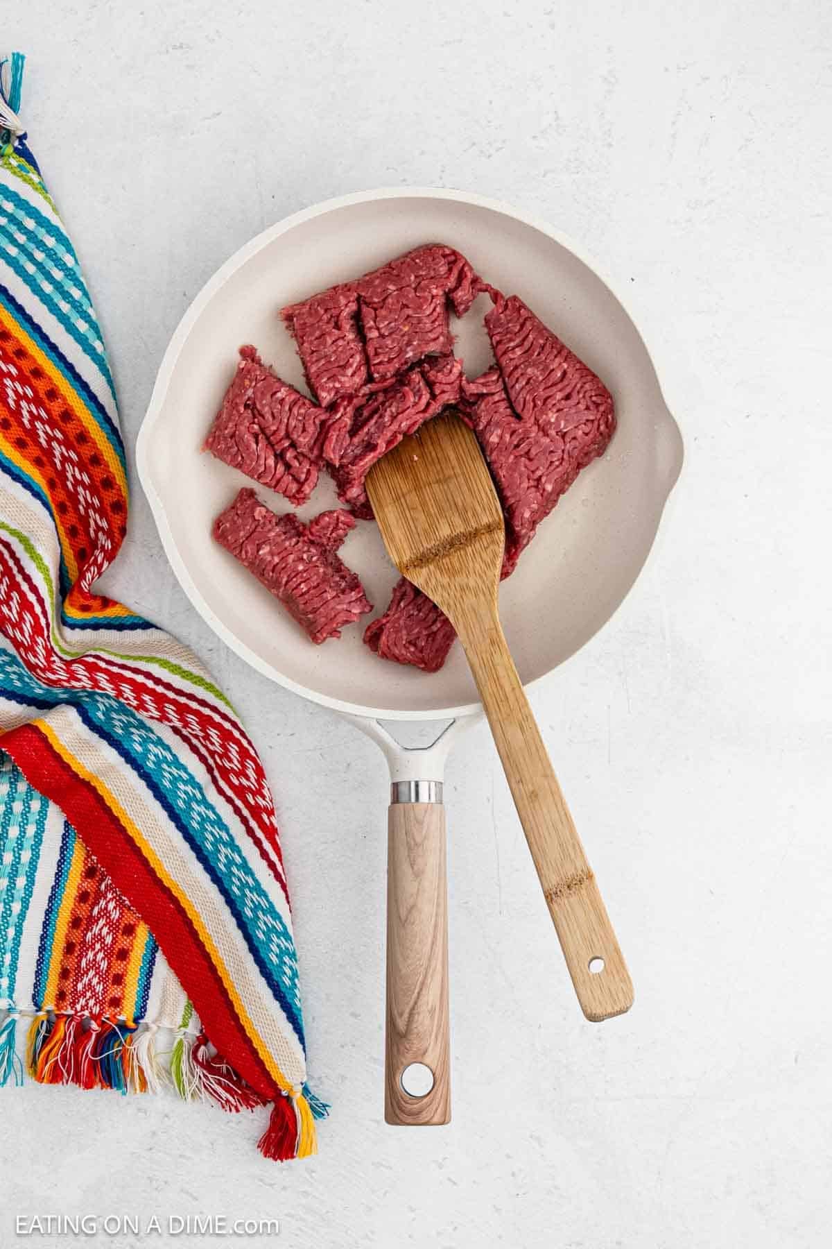 Cooking ground beef in a large skillet with a wooden spoon.