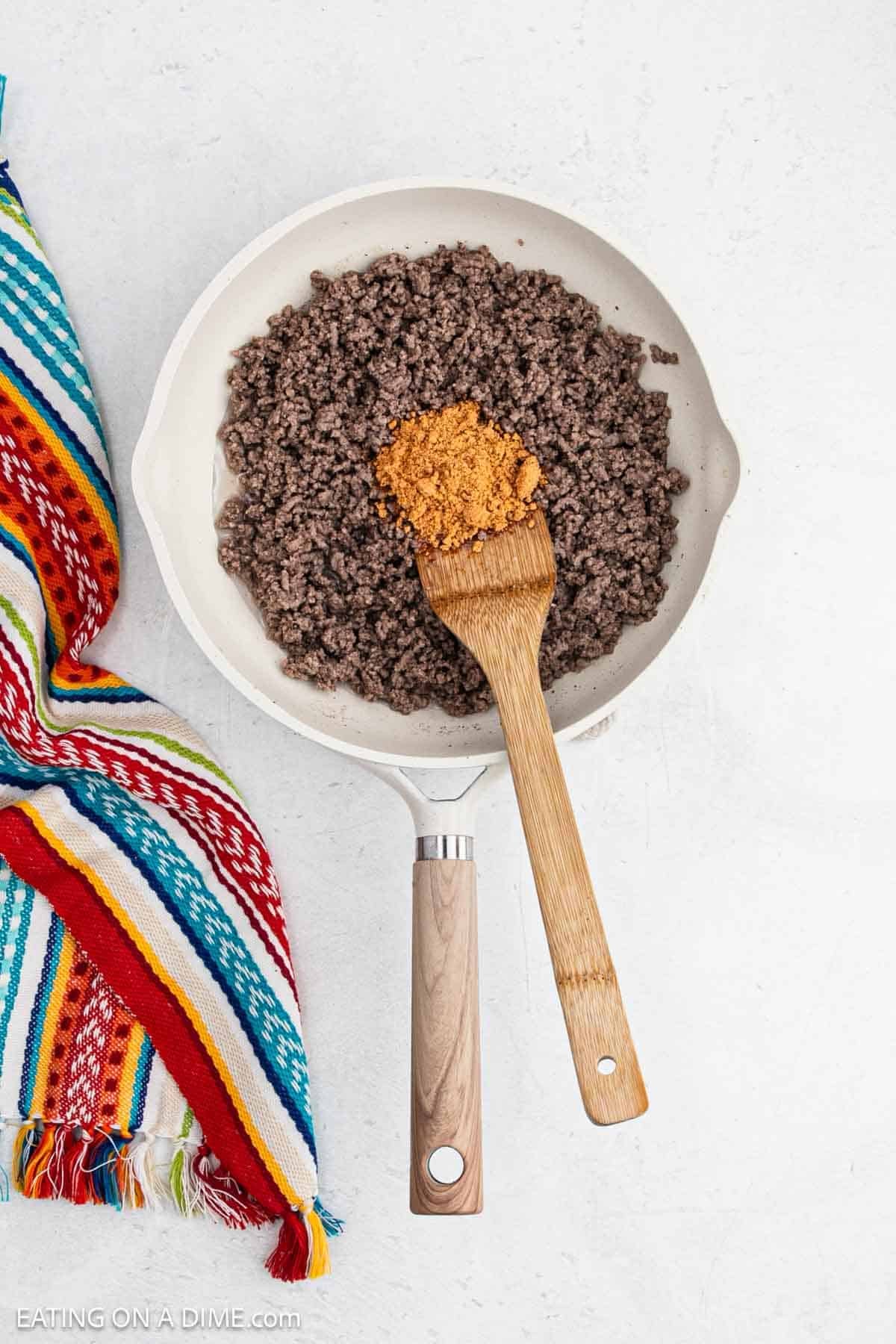 Cooked ground beef in a skillet topped with taco seasoning.