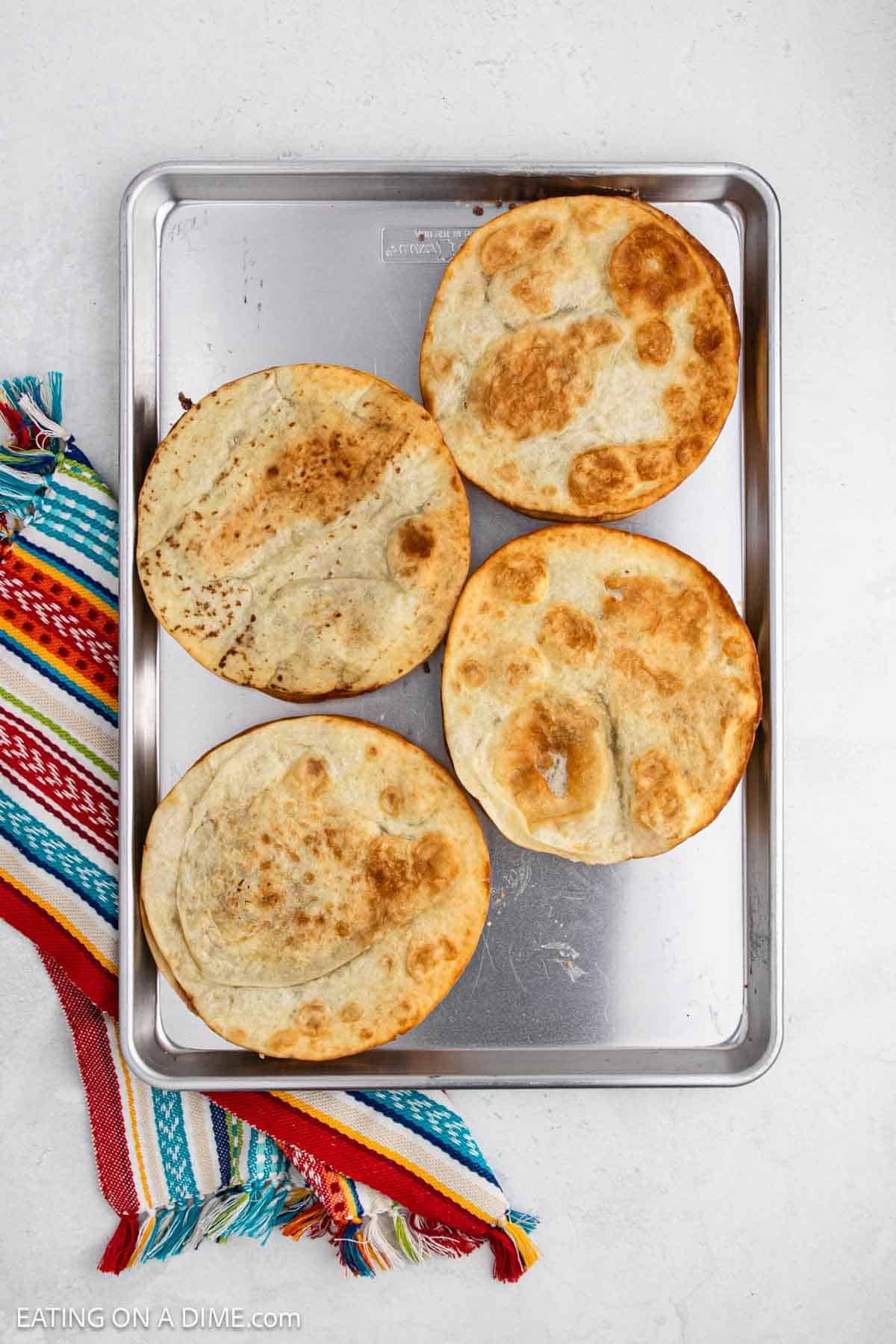 Crispy tortillas placed on the refried beans and ground beef tortillas on a baking sheet.