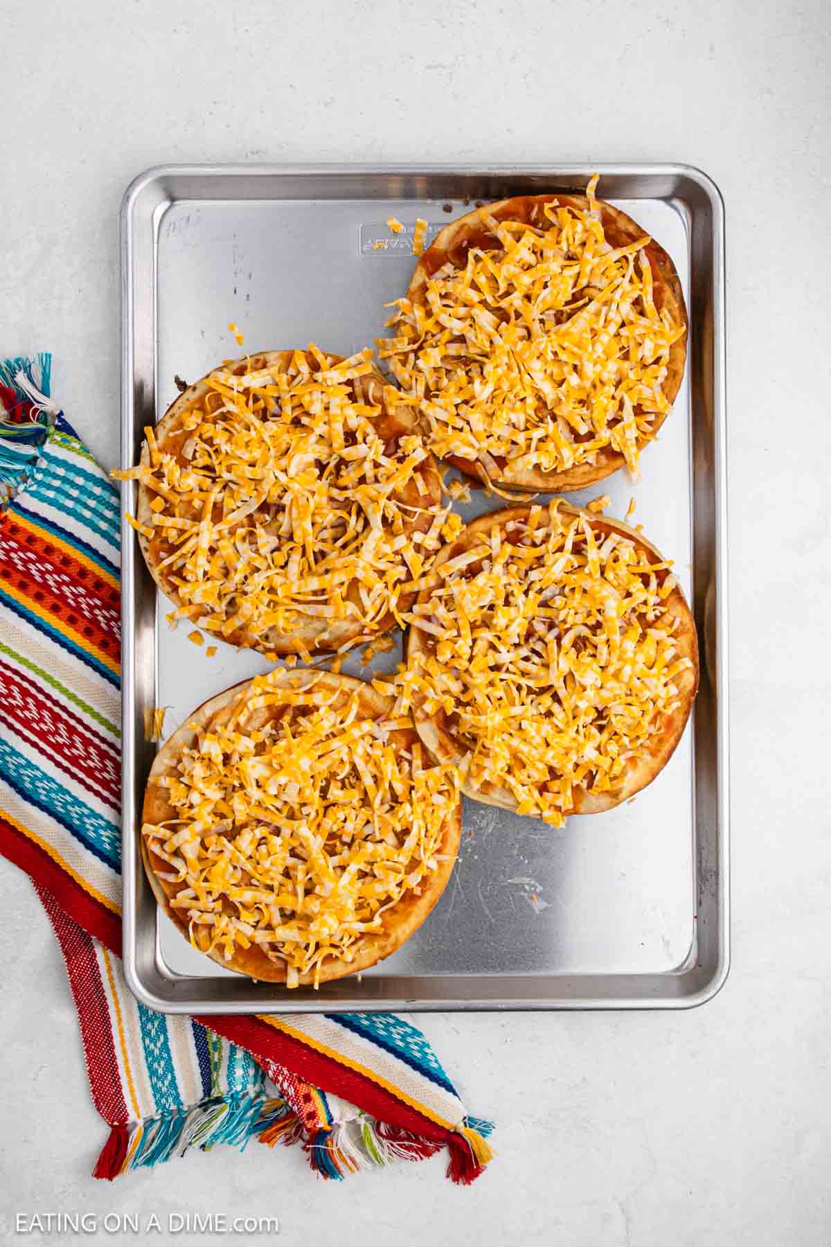 Shredded cheese placed on the tortillas that are covered with red sauce.