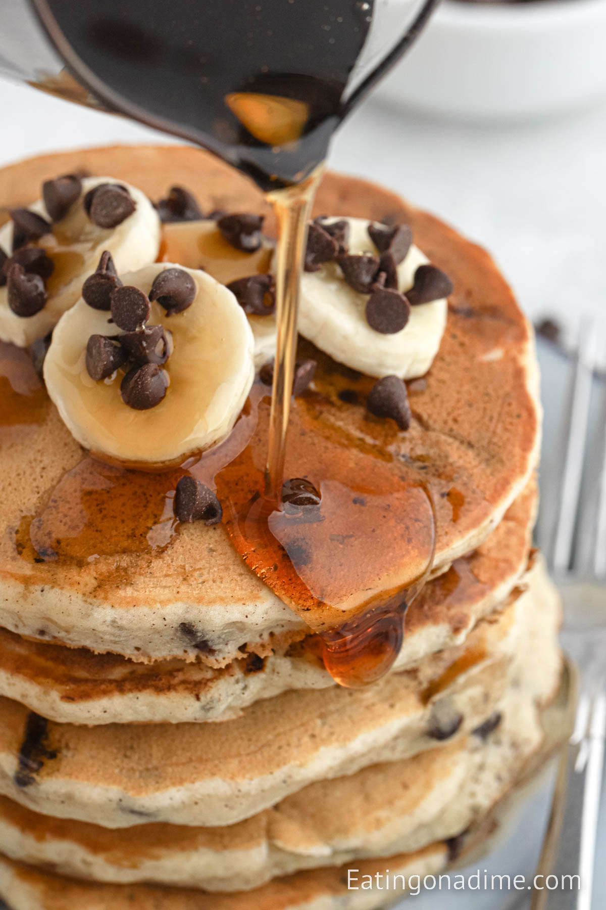 Stacked Banana Chocolate Chip Pancakes on a plate with syrup being over the top
