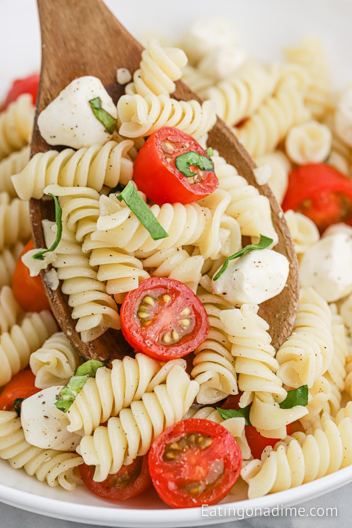 Caprese Pasta Salad in a bowl with a wooden spoon