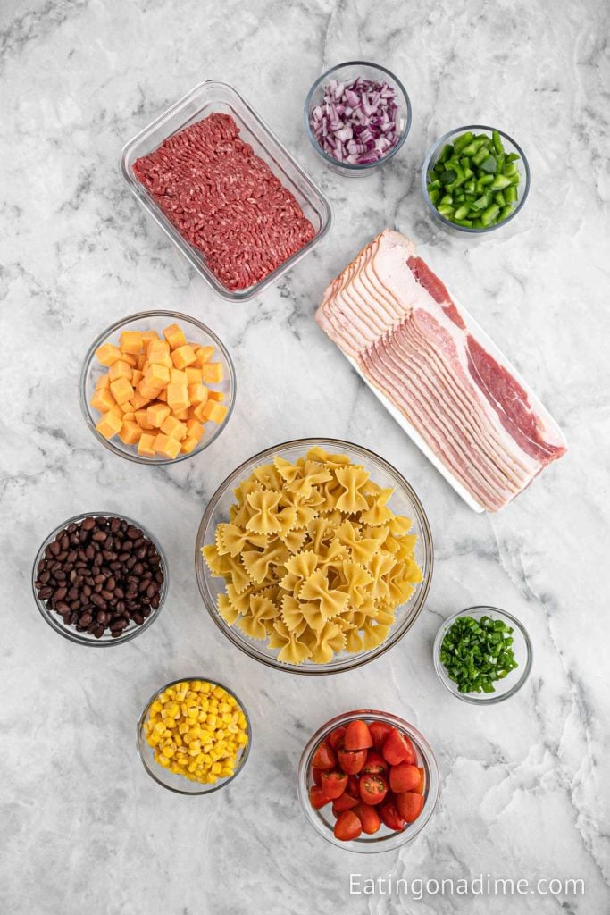 Pasta salad ingredients - bacon, ground beef, pasta, corn, black beans, tomatoes, cheese, onion, bell pepper, onions