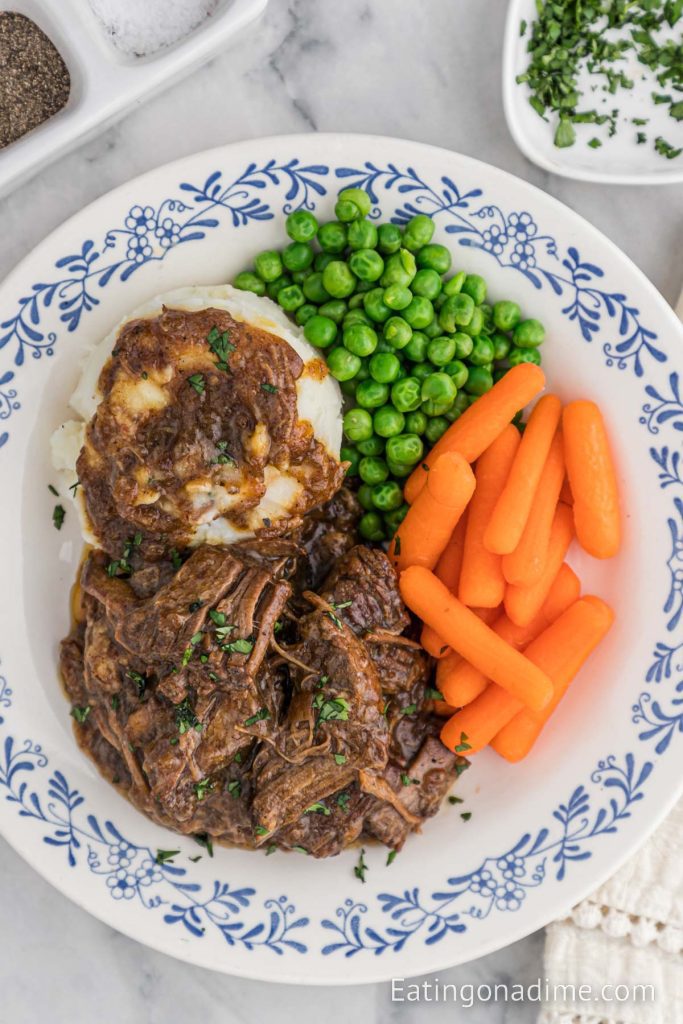 Roast on a plate with mashed potatoes and gravy with peas and carrots