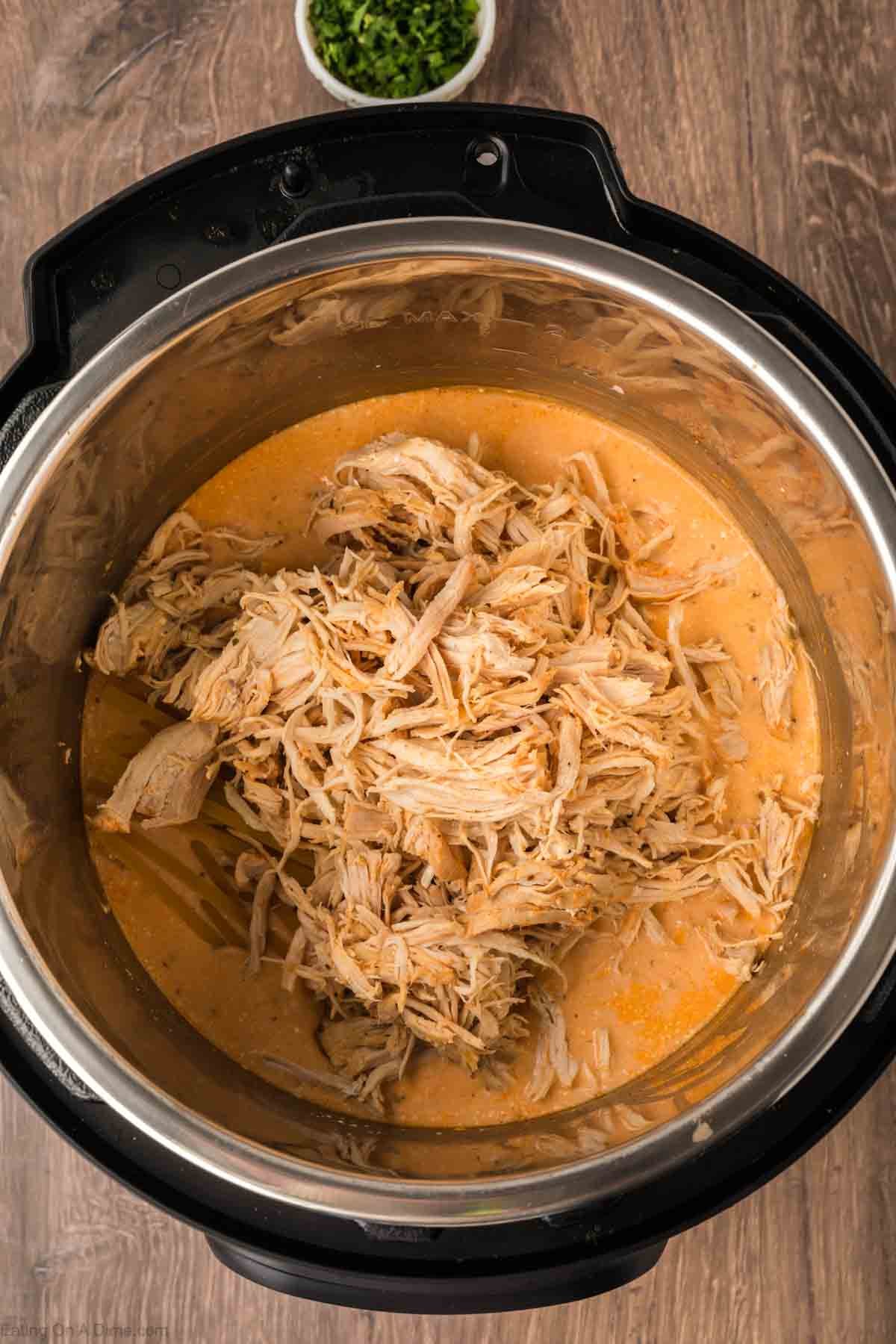Shredded chicken mixed with a creamy orange sauce for Instant Pot Buffalo Chicken Pasta sits on a wooden surface, with a small bowl of chopped herbs in the background.