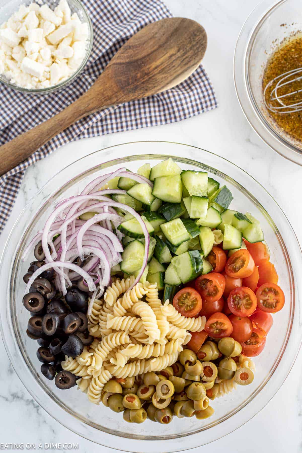 Add in the red onions, slice black olives, cucumbers, cherry tomatoes, olives with the pasta in a bowl