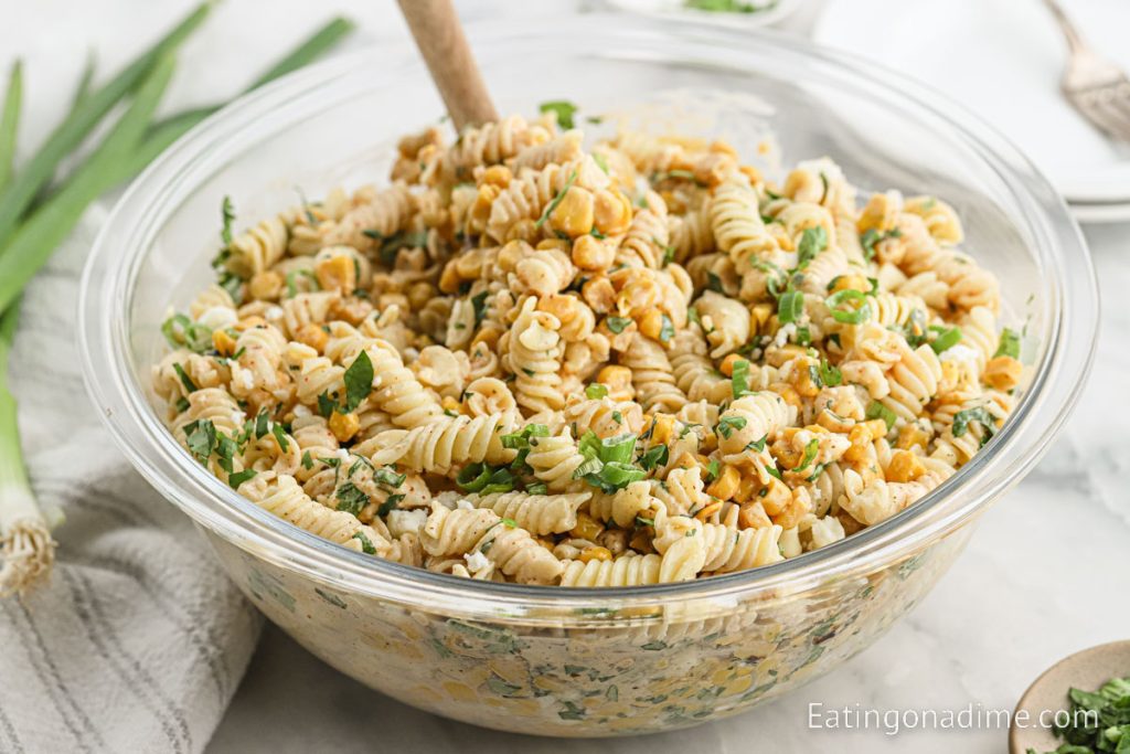 A bowl of Mexican Street Corn Pasta Salad with a wooden spoon