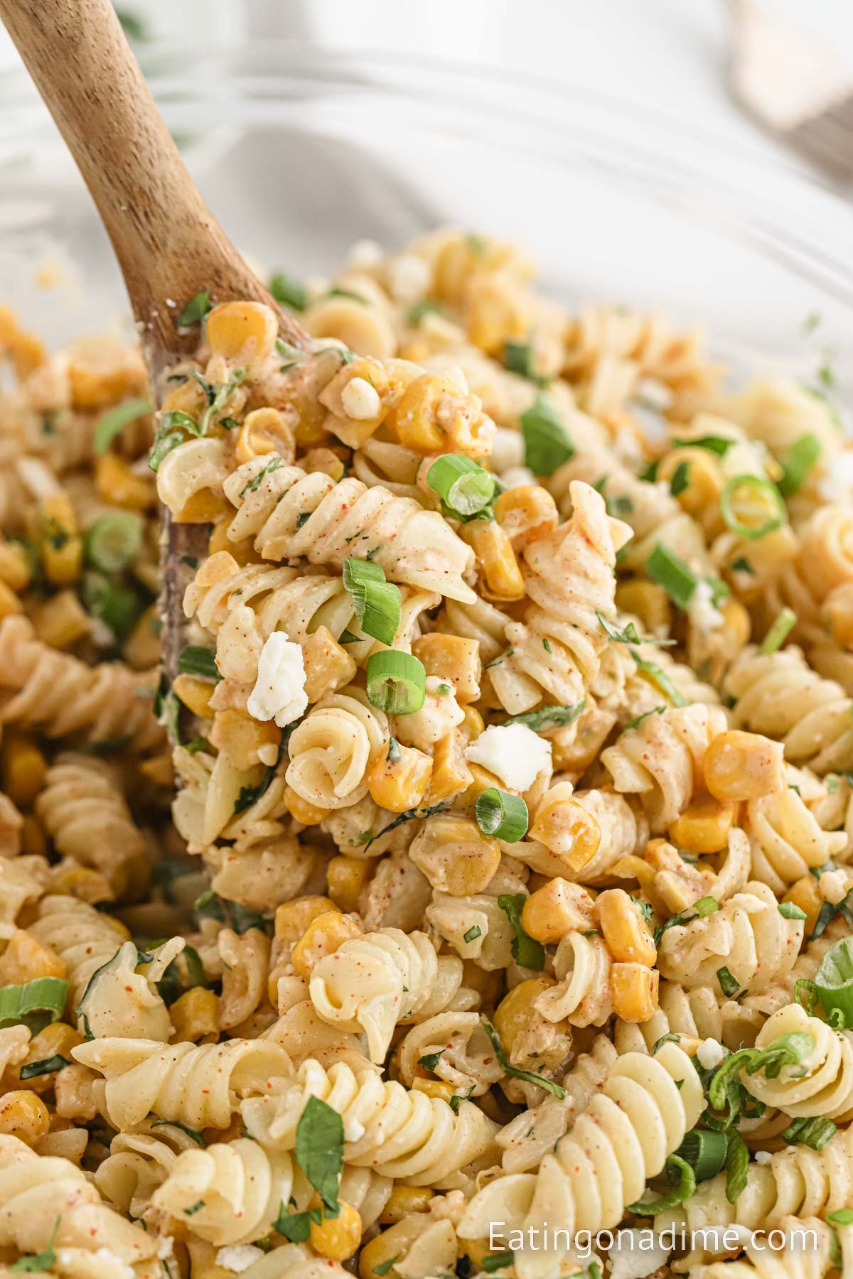 A bowl of Mexican Street Corn Pasta Salad with a wooden spoon