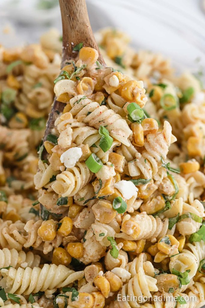 A bowl of Mexican Street Corn Pasta Salad with a wooden spoon