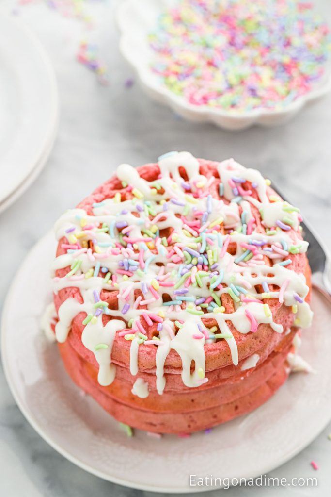 Pink Waffles Stacked on a white plate and topped with glaze and sprinkles