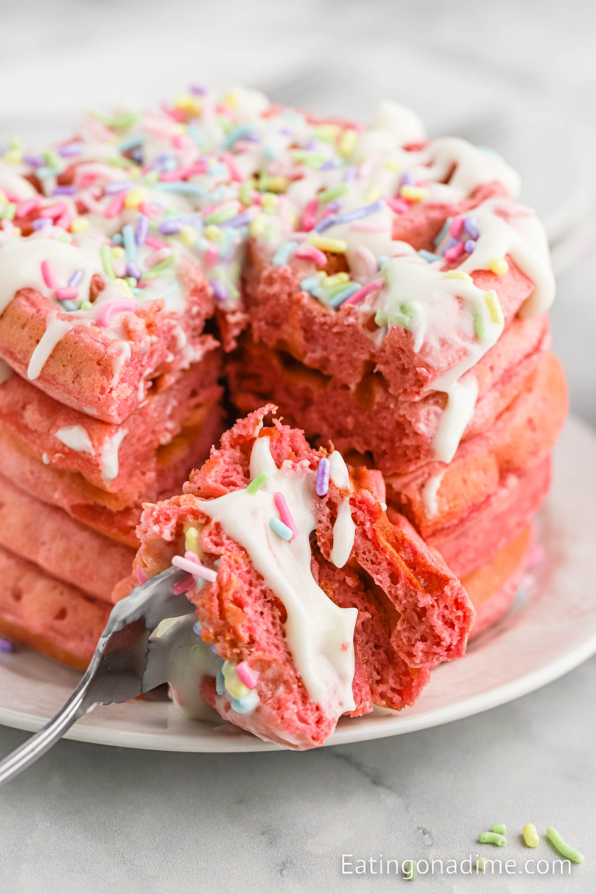 Pink Waffles Stacked on a white plate and topped with glaze and sprinkles