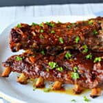 Two racks of glazed barbecue ribs, made using a Slow Cooker Ribs Recipe and garnished with chopped parsley, are served on a white plate, showcasing a rich, sticky sauce and tender meat.