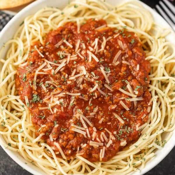 Spaghetti sauce over a bowl of spaghetti noodles topped with parmesan cheese.