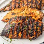 Grilled chicken breasts with dark char marks and a slightly caramelized surface from a Balsamic Chicken Marinade, garnished with chopped herbs and served on a white plate.