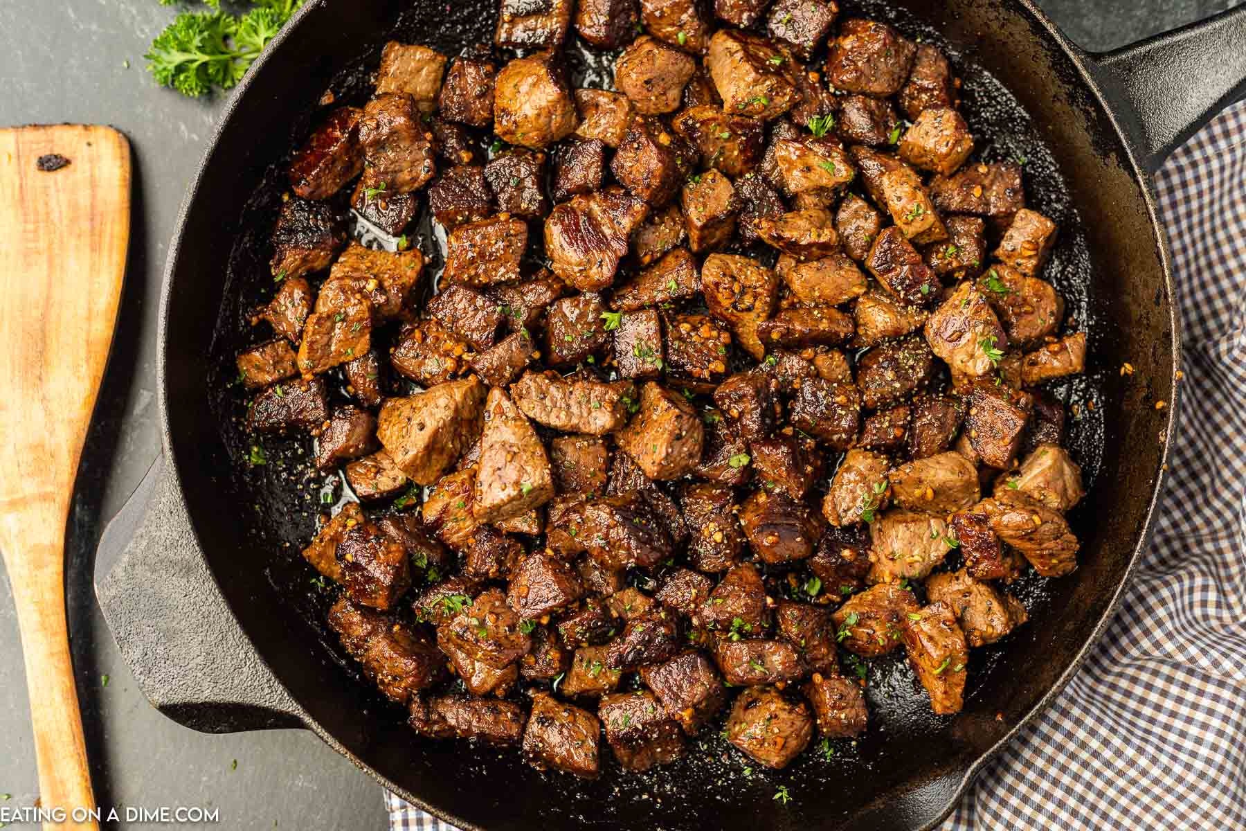 Steak Bites in a cast iron skillet with a wooden spoon on the side