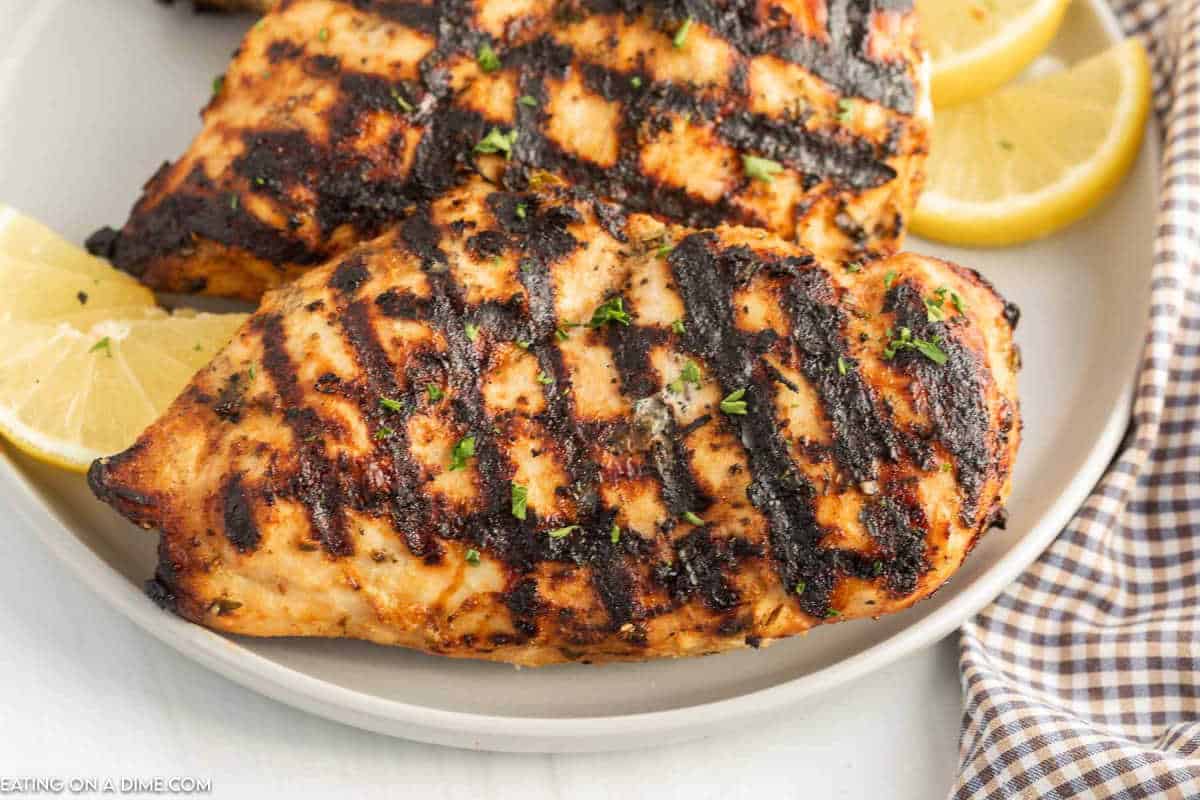 Grilled chicken stacked on a plate with lemon wedges on the side.