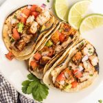 3 chicken tacos topped with pico de gallo on a plate.