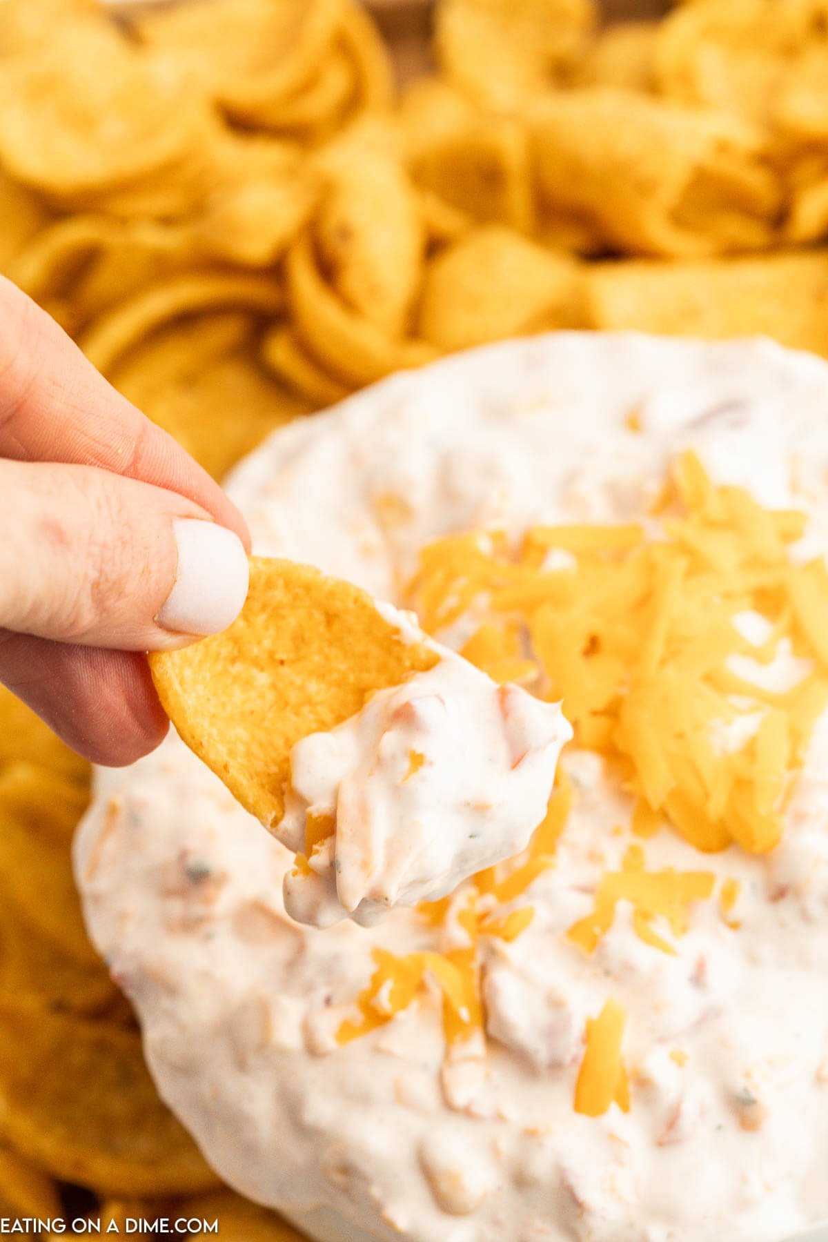 Fiesta Ranch Dip topped with cheese in a bowl with a side of corn chips