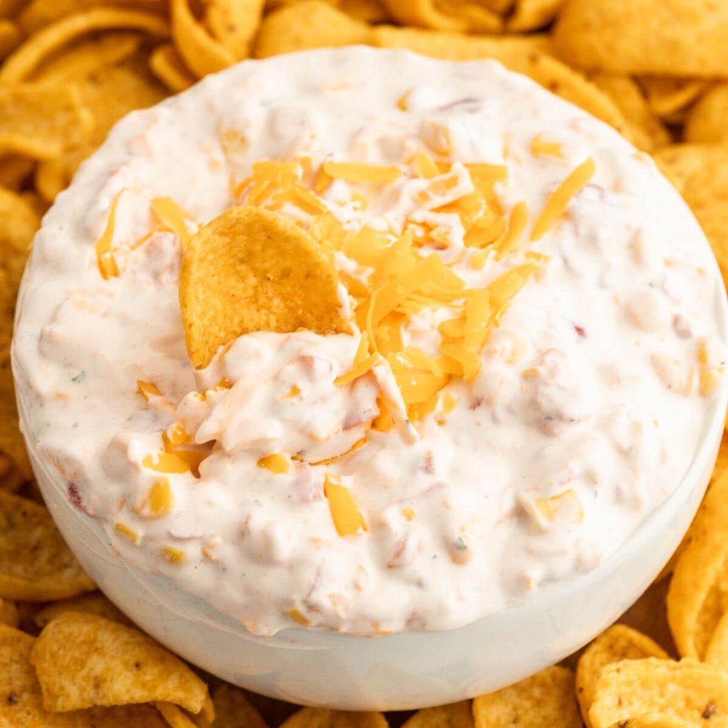 Fiesta Ranch Dip topped with cheese in a bowl with a side of corn chips