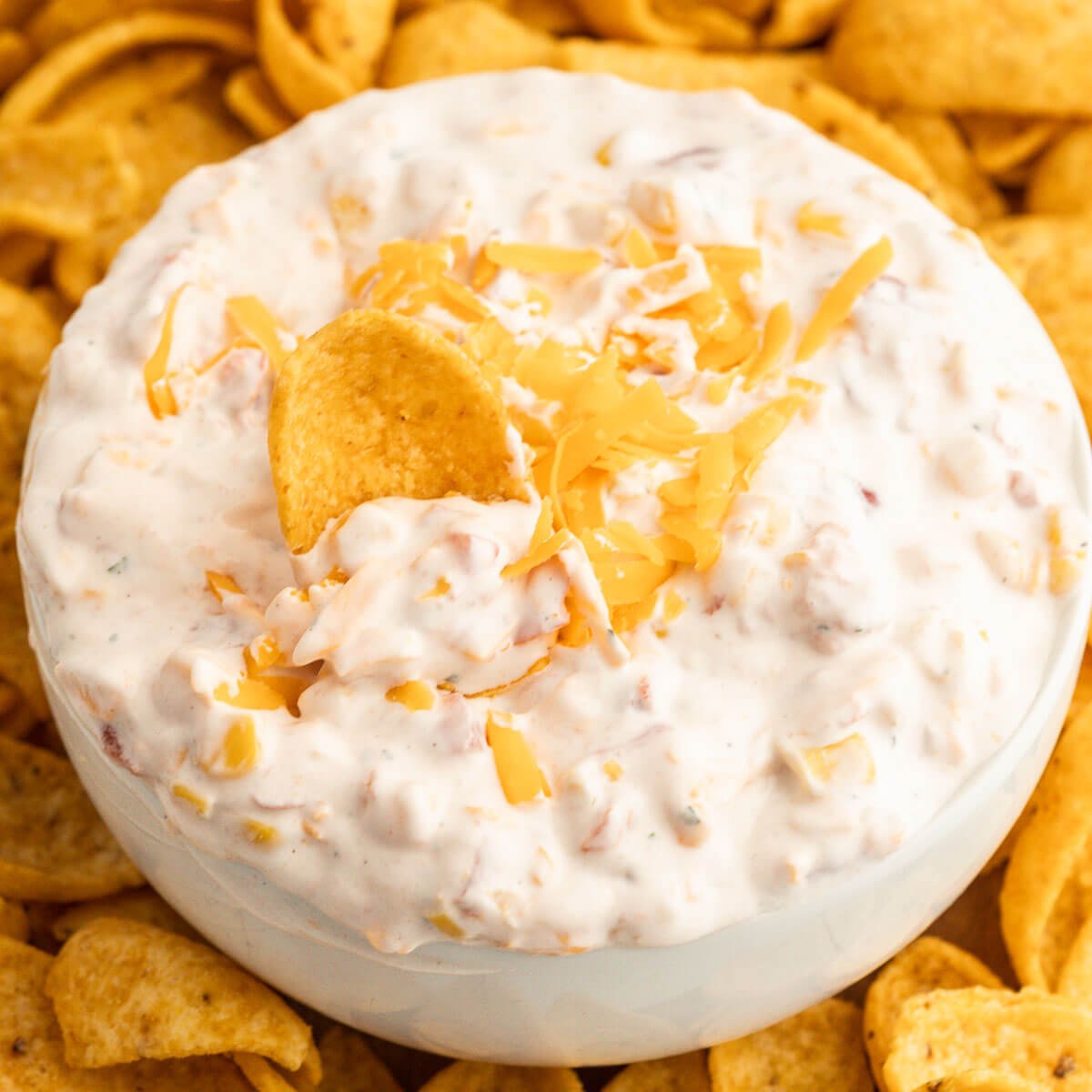 Fiesta Ranch Dip topped with cheese in a bowl with a side of corn chips