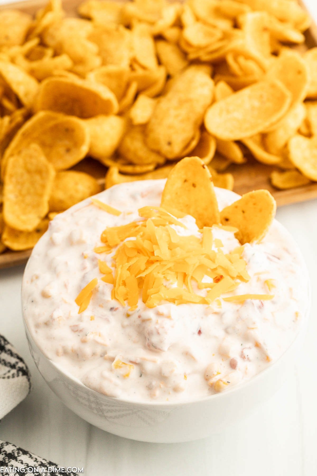 Fiesta Ranch Dip topped with cheese in a bowl with a side of corn chips