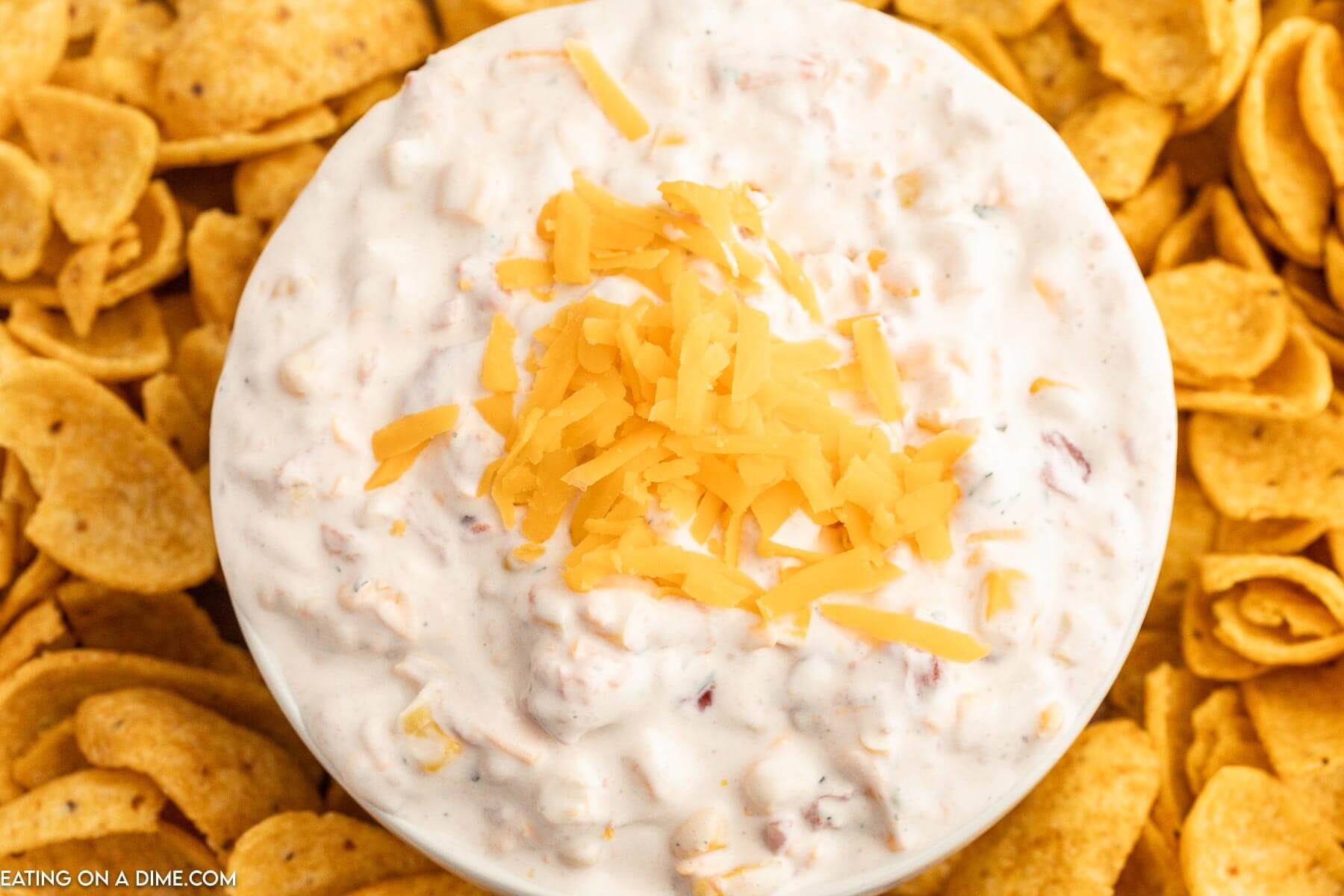 Fiesta Ranch Dip topped with cheese in a bowl with a side of corn chips