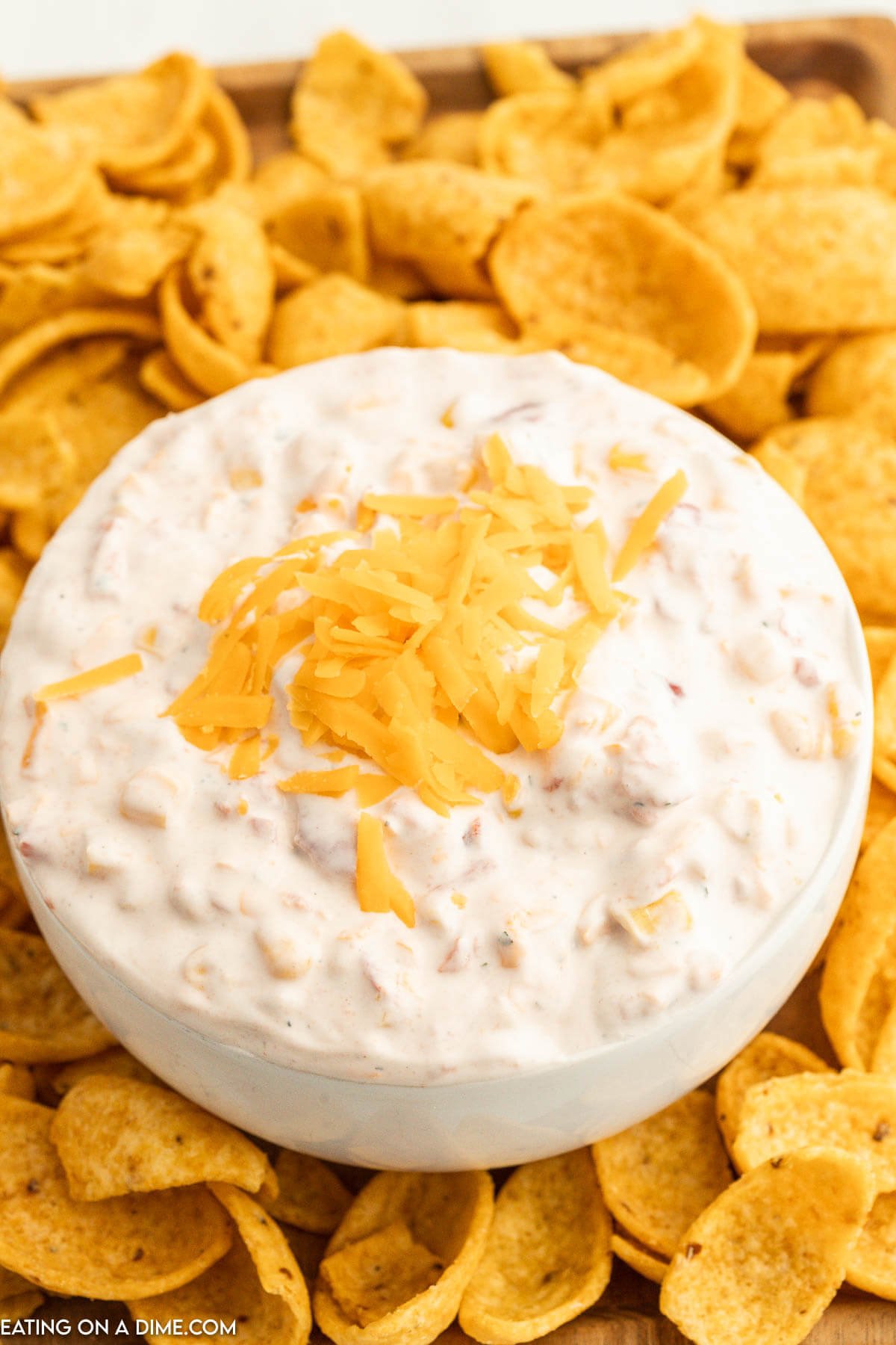 Fiesta Ranch Dip topped with cheese in a bowl with a side of corn chips