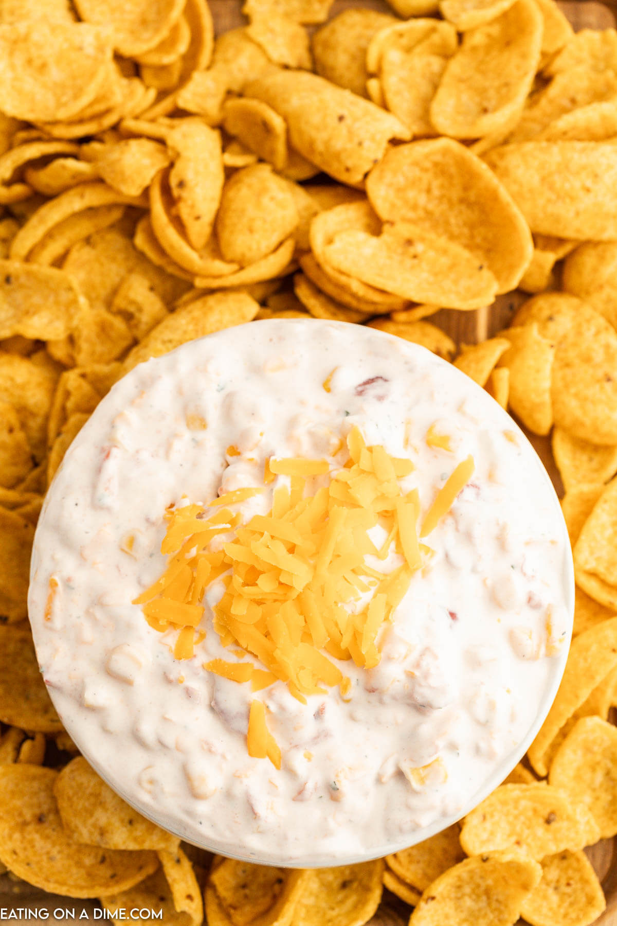 Fiesta Ranch Dip topped with cheese in a bowl with a side of corn chips