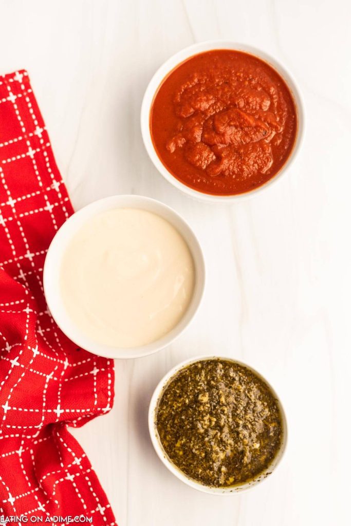 Bowls of alfredo sauce, marinara sauce, and a pesto sauce