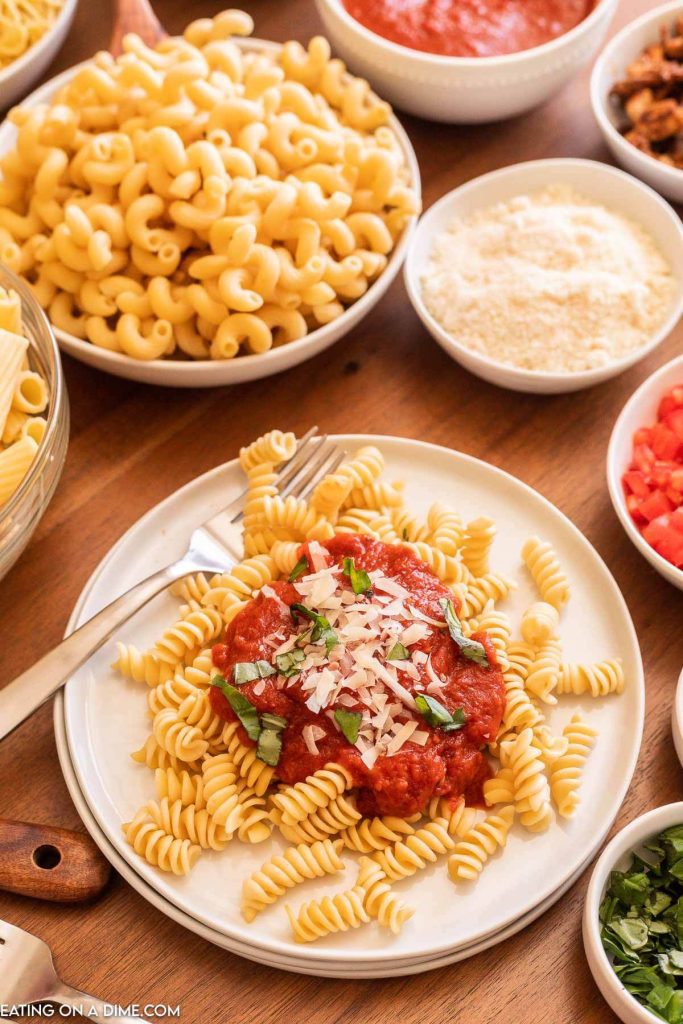 Rotini pasta with tomato sauce on top and bowls of noodles and other toppings