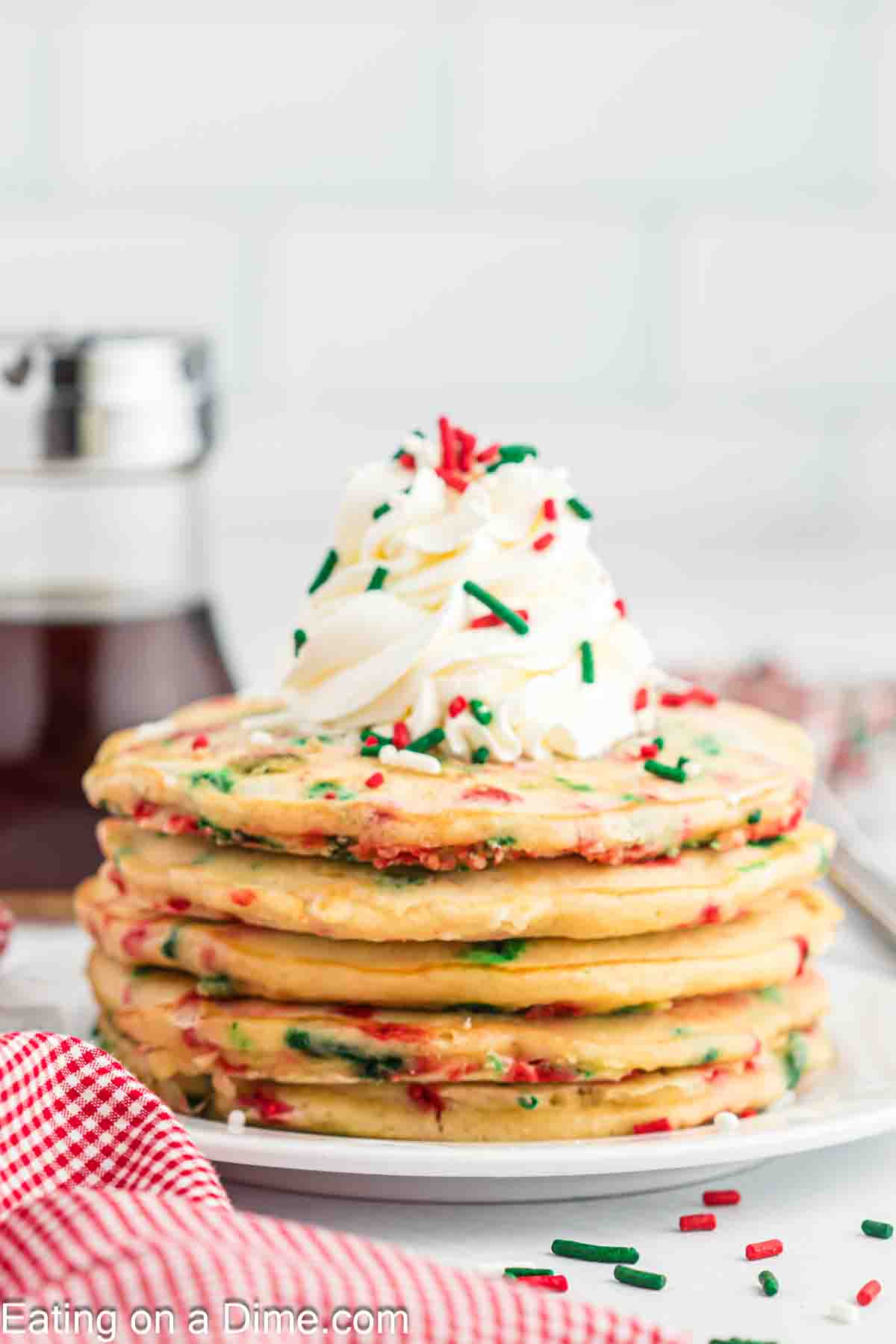 Christmas Pancakes Stacked on a platter topped with whipped cream and sprinkles