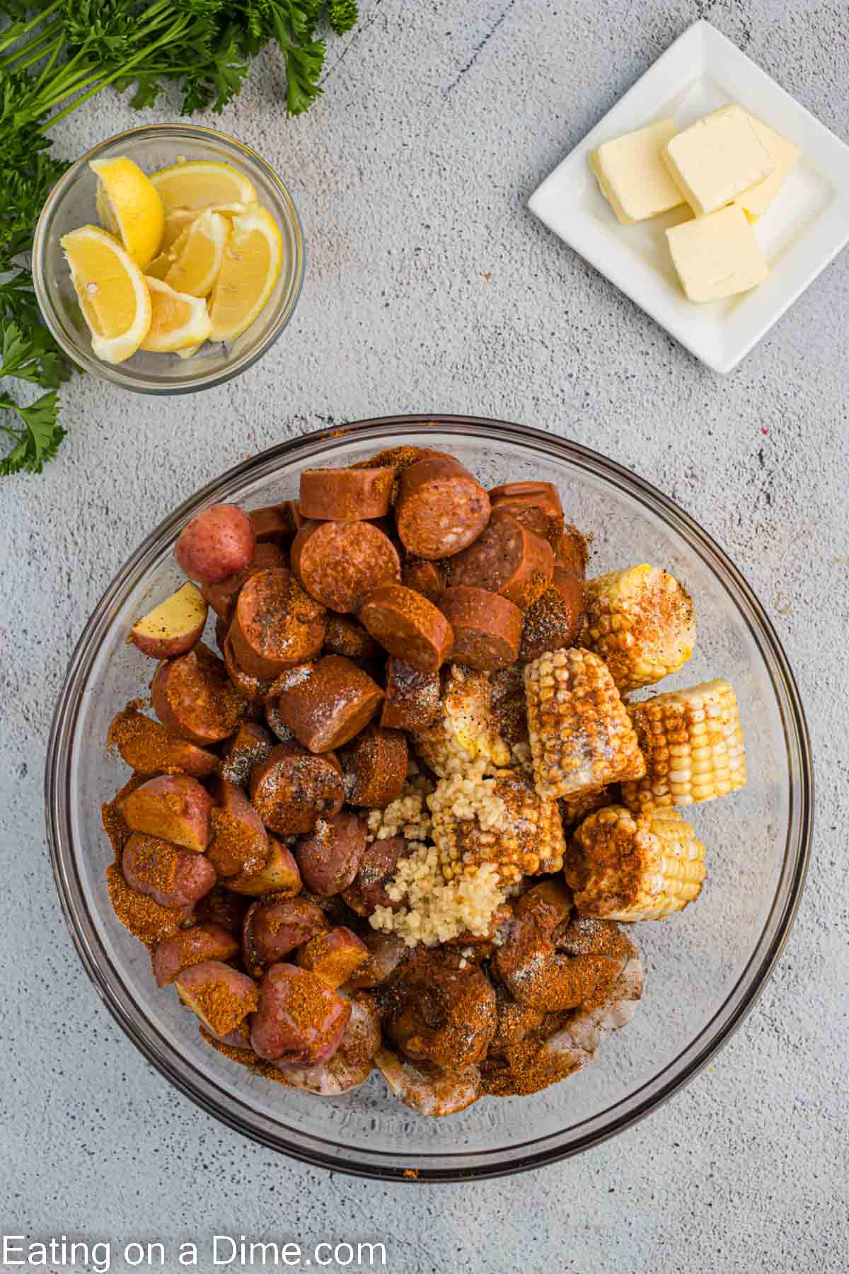Mixing the minced garlic and seasoning with the shrimp, sausage and corn and potatoes