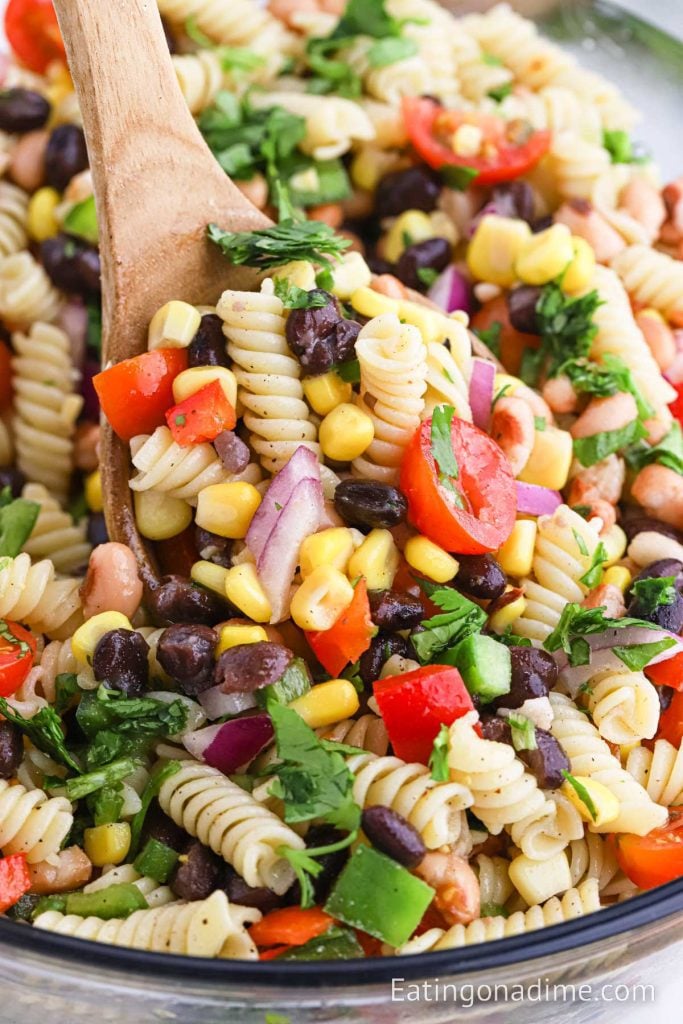 A bowl of Cowboy Caviar Pasta Saald with a wooden spoon