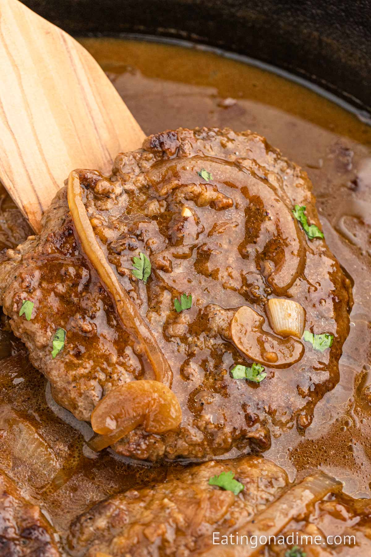 Cube Steak and gravy in a skillet with a wooden spoon